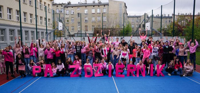 Uczniowie XIII LO ubrani na różowo podczas wspólnego zdjęcia na boisku szkolnym.
